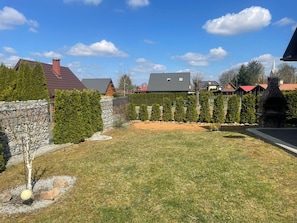 A residential area with a stone wall, a lawn, and a row of evergreen trees. - Comfortable Holiday Home, Close to the Lake (Lubrza)