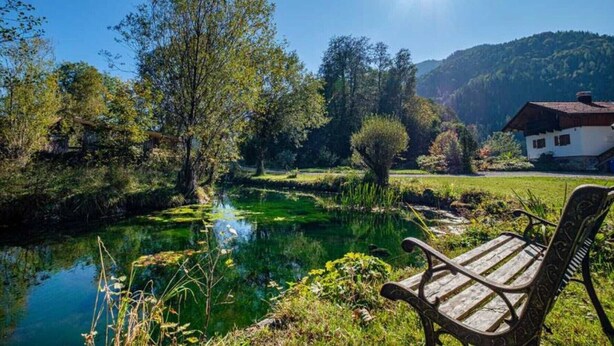 Un cadre paisible au bord d’un lac, avec un banc en bois, une maison en arrière-plan et un ciel dégagé.