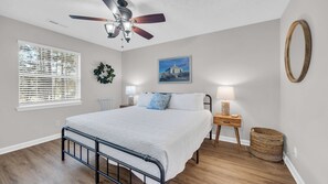 A bedroom with a bed, a ceiling fan, a window with blinds, a nightstand with a lamp, a wall-mounted mirror, and a woven basket. - TB 6E Palmetto Paradise TB 6E 2Br/2BA condo located in Pawleys Island (Pawleys Island)