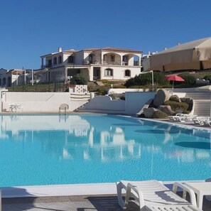 A swimming pool with lounge chairs and umbrellas, surrounded by a landscaped area with rocks and a building in the background. - Apartment With sea View and Great Roof Terrace (Santa Teresa di Gallura)