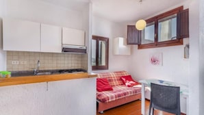 A compact kitchen with white cabinets, a tiled backsplash, and a small dining area with a table and chair. - Apartment With sea View and Great Roof Terrace (Santa Teresa di Gallura)