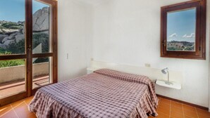 A bedroom with a bed, a nightstand, a desk, and a window with a view of rocks and greenery. - Apartment With sea View and Great Roof Terrace (Santa Teresa di Gallura)