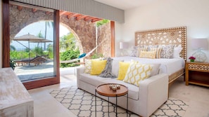 A hotel room with a bed, a sofa, a small table, and a view of a tropical outdoor area. - Casa Serena in Punta Mita (Punta de Mita)