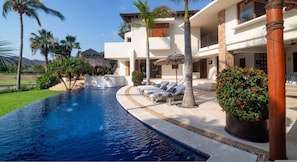 A poolside area with lounge chairs, a palm tree, and a building with a balcony. - Casa Serena in Punta Mita (Punta de Mita)