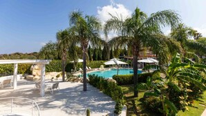 A pool area with lounge chairs and umbrellas, surrounded by palm trees and greenery. - Studio for Couples in Capo Vaticano With Pool (Ricadi)