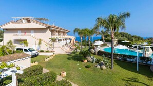 A house with a swimming pool, palm trees, and a clear view of the ocean. - Studio for Couples in Capo Vaticano With Pool (Ricadi)
