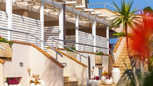 A modern building with a staircase, outdoor seating area, and large planters with flowers. - Studio for Couples in Capo Vaticano With Pool (Ricadi)