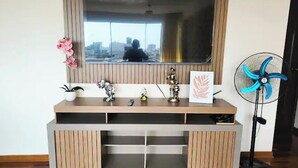 Un soggiorno moderno con TV a incasso, mobile TV in legno, oggetti decorativi e una ventola da pavimento.