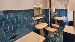 A modern bathroom with a bathtub, two sinks, and a bidet. The walls are tiled in blue, and there is a large mirror above the sink. - Family home, sleeps 8, terrace with panoramic view in Porquerolles (Hyères)