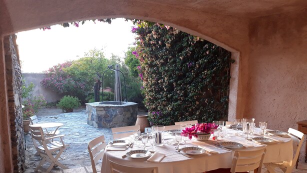 An outdoor dining area with a stone fire pit, white chairs with red cushions, and a table set for four. - Family home, sleeps 8, terrace with panoramic view in Porquerolles (Hyères)