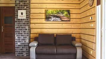 Un interior de madera con un sofá, una pared de ladrillo y una imagen de un arroyo.