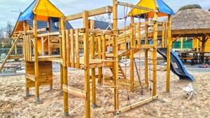 A wooden playground structure with climbing elements and a slide, set on sandy ground. - Holiday Home With a Terrace, Close to the Lake (Lubrza)