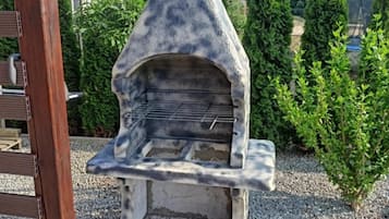 Un horno de piedra al aire libre con una rejilla metálica, rodeado de grava y follaje.