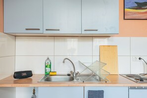A kitchen with a sink, a JBL speaker, a dish rack, and a cutting board. - Spacious design apartment near the Estrel Hotel (Berlin)