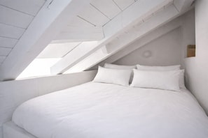Ein Schlafzimmer mit schrägem Dach und Dachfenster, mit einem Bett mit weißer Bettwäsche.