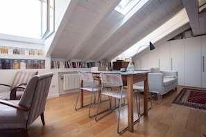 Ein Loft-Zimmer mit Essbereich, Bücherregalen und Blick durch ein Dachfenster.