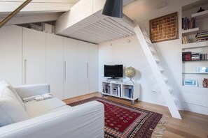 Ein modernes Wohnzimmer mit einem weißen Sofa, einem roten Teppich mit Muster, einem Fernseher, einem Globus und einem Bücherregal.
