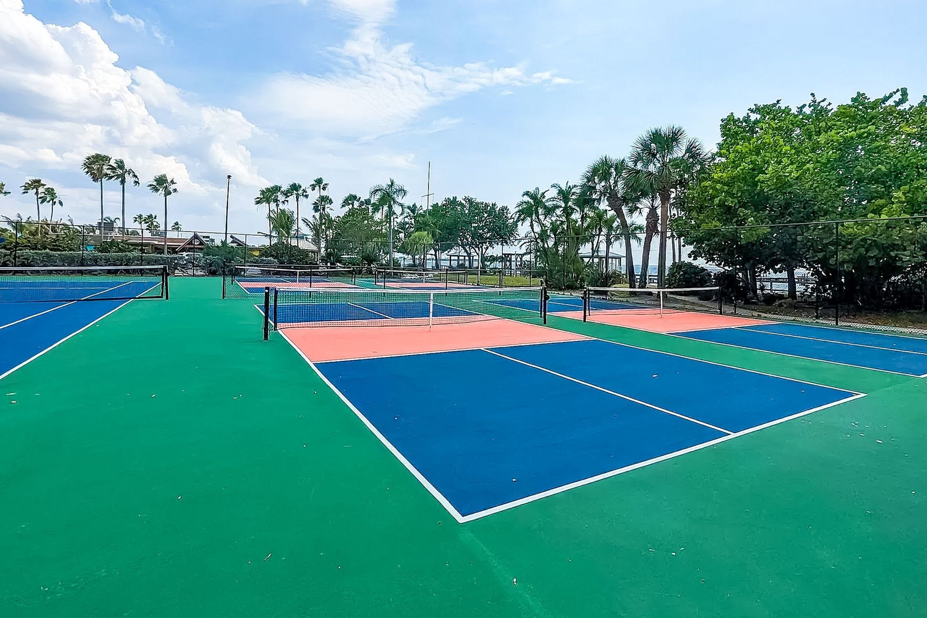 A tennis court with multiple courts, surrounded by palm trees and a clear sky.