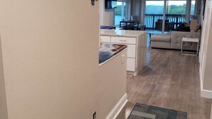 A hallway leading to a living area with a kitchen, a dining area, and a view of the outdoors. - Waterfront Balcony Condo Beach Access Hot Tub (Ruskin)