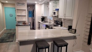 A modern kitchen with white cabinets, a marble countertop, and two bar stools. - Waterfront Balcony Condo Beach Access Hot Tub (Ruskin)