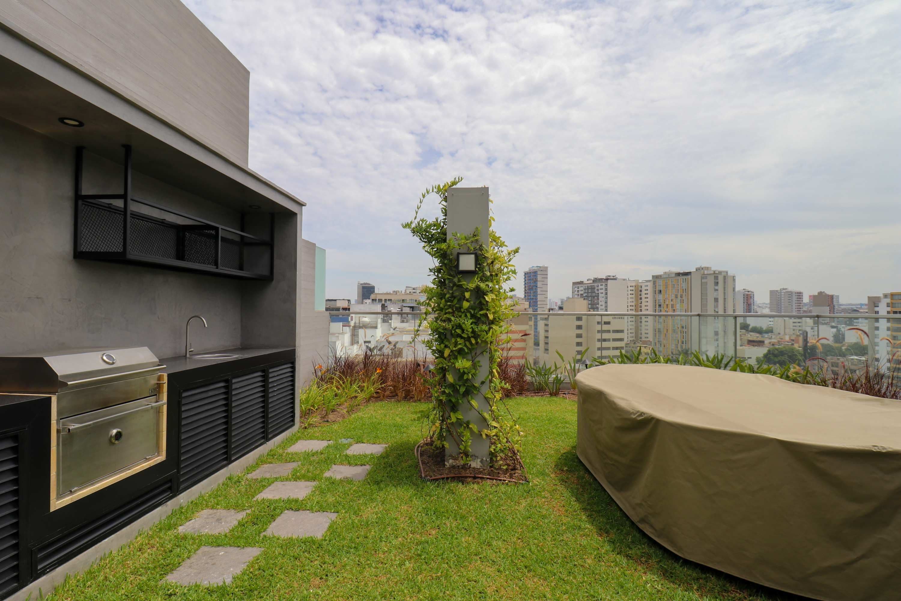 A rooftop terrace with a grill, planter, and city view.