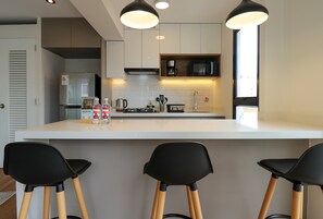 Eine moderne Küche mit einer zentralen Kochinsel, Barhocker, einem Kühlschrank, einer Mikrowelle und einer Kaffeemaschine.