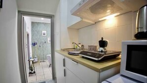 Une cuisine compacte équipée d’un four à micro-ondes, d’un grille-pain et d’une bouilloire sur le plan de travail. Un petit réfrigérateur est visible sur la droite. La cuisine est dotée d’un dosseret carrelé et d’une bouche d’aération au plafond.