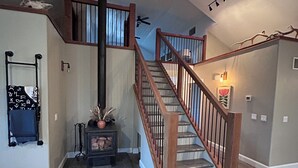 A spacious living area with a wooden staircase, a fireplace, and a ceiling fan.