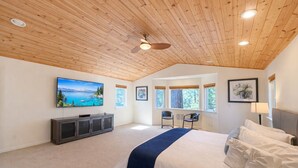 A bedroom with a large bed, a TV, a ceiling fan, and windows with a view of trees. - NEW property Private Skyland Beach,Modern Zephyr Cove Retreat,Hot Tub(ZC1034) (Zephyr Cove)