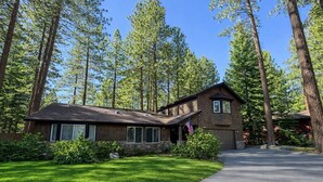 A two-story house with a stone foundation, a sloped roof, and a garage. It is surrounded by tall pine trees and has a well-maintained lawn. - NEW property Private Skyland Beach,Modern Zephyr Cove Retreat,Hot Tub(ZC1034) (Zephyr Cove)
