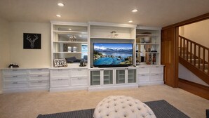 A living room with a large flat-screen TV, white cabinetry, a tufted ottoman, and a staircase. - NEW property Private Skyland Beach,Modern Zephyr Cove Retreat,Hot Tub(ZC1034) (Zephyr Cove)