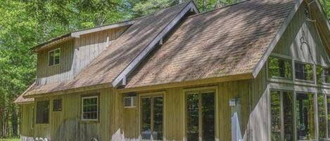 Une cabane en bois rustique, dotée d’un toit à pignon, de grandes fenêtres et d’une véranda.