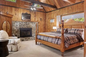 A wooden cabin bedroom with a stone fireplace, a four-poster bed, and a view of the outdoors through a window. - Stargazer Shores Limit 8 4 Bedroom Home (Bridgton)