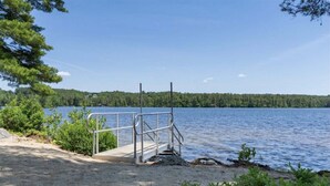 Hiekkainen ranta, josta metalliset portaat johtavat veteen. Rantaa ympäröi vehreää kasvillisuutta ja sen vieressä on metsäinen rantaviiva.