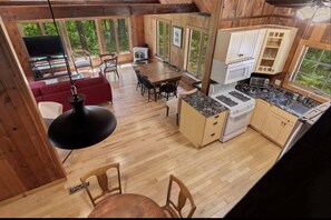 A wooden cabin interior with a dining area, kitchen, and living space. - Stargazer Shores Limit 8 4 Bedroom Home (Bridgton)