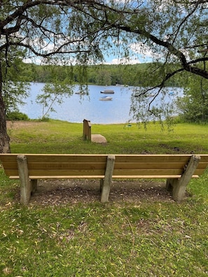 A wooden bench in a park with a lake and boats in the background.