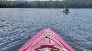 A pink kayak with a bottle and a whistle on the bow, heading towards another kayak on calm water with a forested shoreline in the background. - Wildflower Cabins Limit 6 3 Bedroom Villa (Naples)