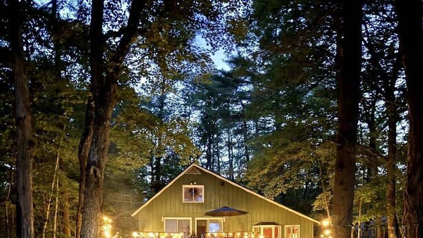 A rustic cabin with a deck, surrounded by trees. - Upta Camp Limit 8 3 Bedroom Cabin (East Baldwin)