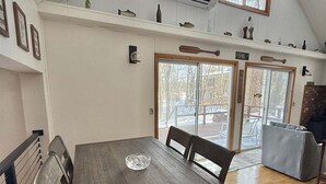 A dining area with a wooden table and chairs, a bench, a glass-top table, and a view of the outdoors through large glass doors. - Upta Camp Limit 8 3 Bedroom Cabin (East Baldwin)