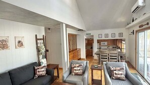 A spacious living room with a high ceiling, wooden flooring, and a mix of grey sofas and a dark sofa. - Upta Camp Limit 8 3 Bedroom Cabin (East Baldwin)