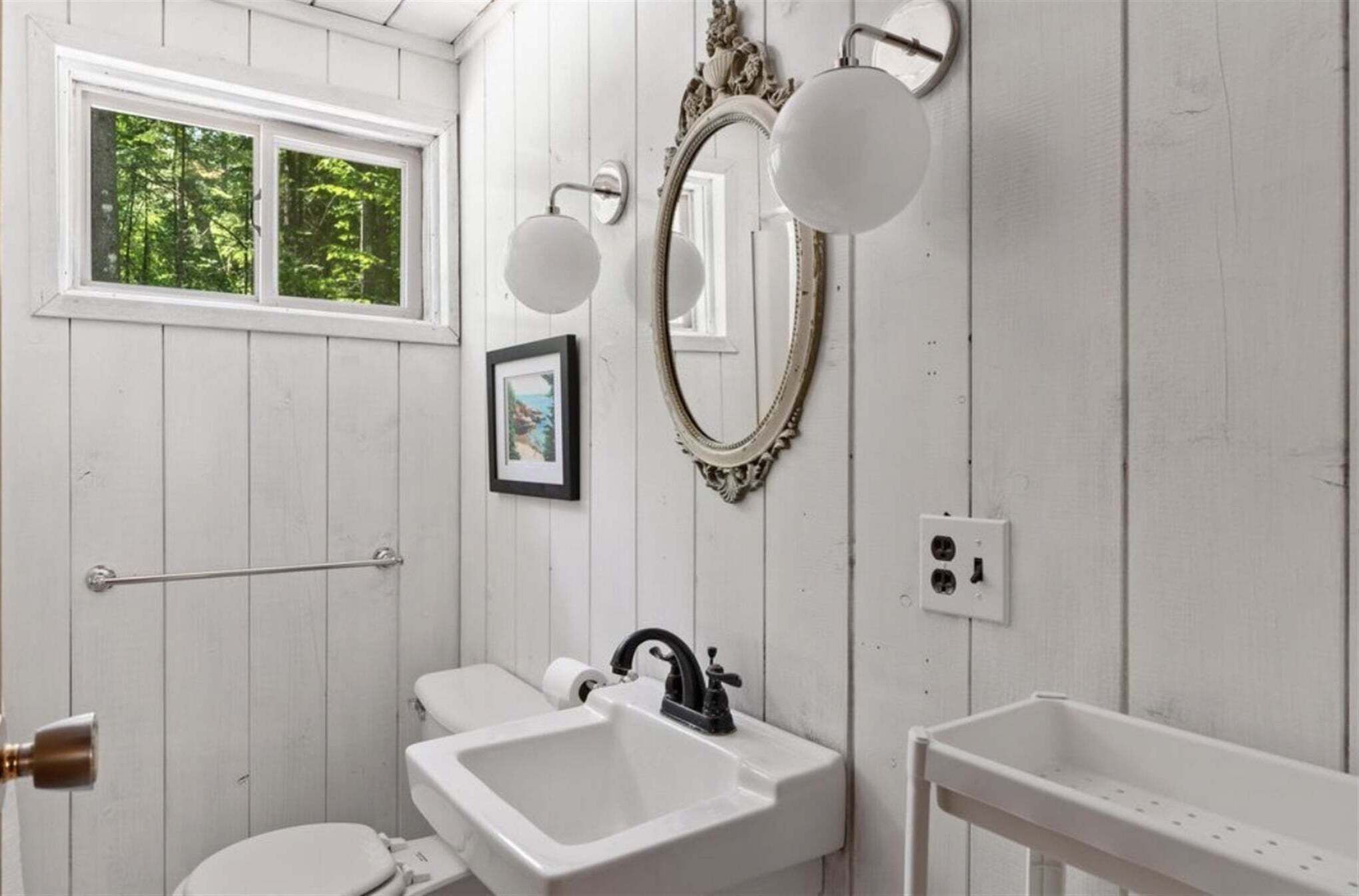 A bathroom with a window, a sink, a toilet, and a mirror.