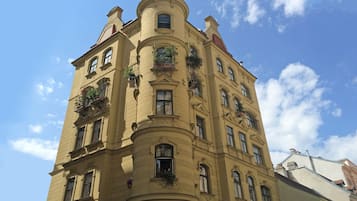 Ein mehrstöckiges Gebäude mit abgerundeter Ecke, zahlreichen Fenstern und Balkonen mit Pflanzen.