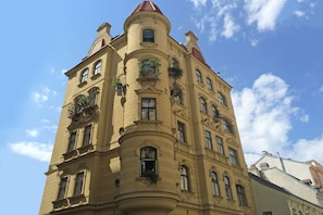 Un immeuble à plusieurs étages, doté d’un coin arrondi, de nombreuses fenêtres et de balcons ornés de plantes.
