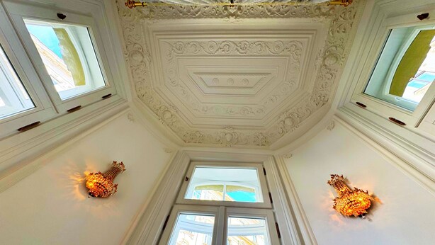 Quarto com teto branco ricamente decorado e três janelas.