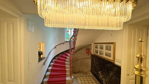 Uma escadaria imponente com tapete vermelho, um candelabro e um extintor de incêndio.