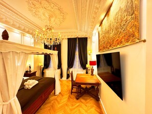 Ein Zimmer mit einem Bett, einem Tisch, einer Chandelüster und einem Gemälde an der Wand.