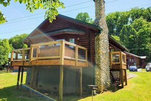A log cabin with a stone exterior, a wooden deck, and a fenced-in area. - Skinny Dippin 2 Bedroom Cabin (Pigeon Forge)