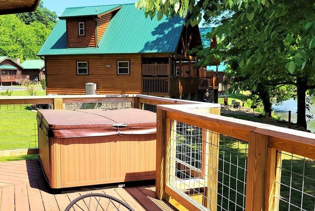 Une cabane en bois avec un toit vert, un jacuzzi et une terrasse délimitée par une clôture.