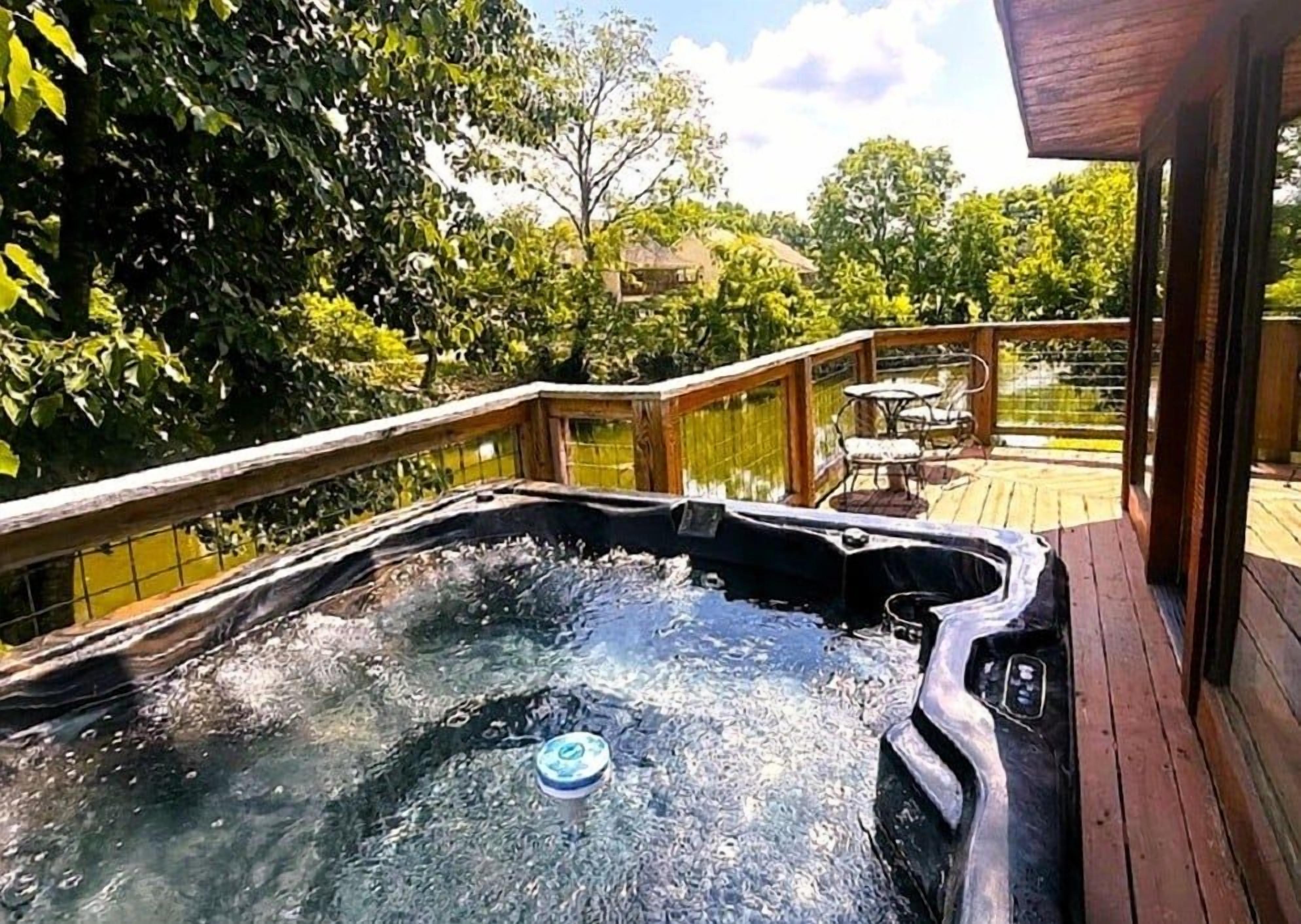 Ein Whirlpool auf einer Holzterrasse mit Blick auf Bäume und ein Gebäude im Hintergrund.