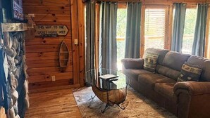 A cozy cabin interior with a stone wall, a wooden floor, a glass-top coffee table, a brown sofa, and a sign indicating a secret fishing hole. - Skinny Dippin 2 Bedroom Cabin (Pigeon Forge)